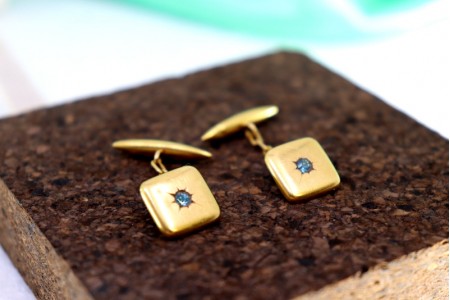 Botões de punho em ouro de formato quadrado e côncavo com zircónias azuladas.